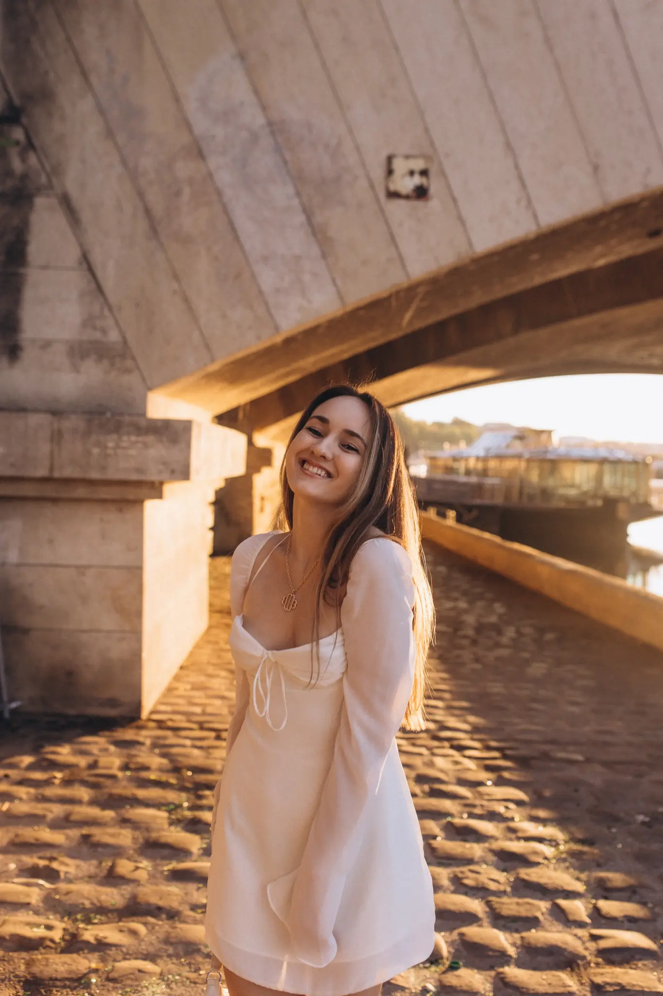 A woman beneath a Parisian bridge arch by the Seine, golden hour light glowing across old cobblestones.
