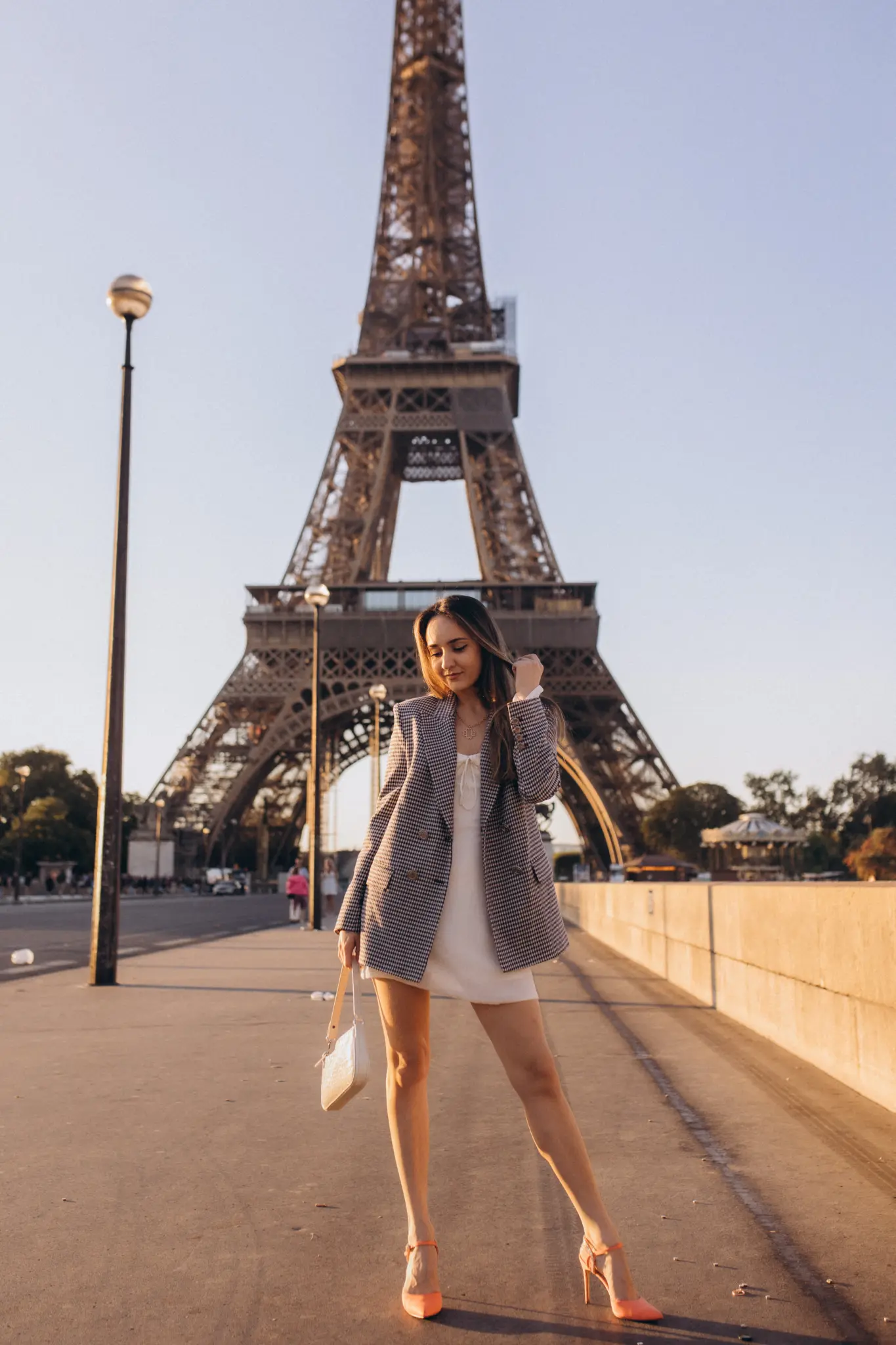A checked blazer over a white dress on a Paris bridge, the Eiffel Tower centered behind.