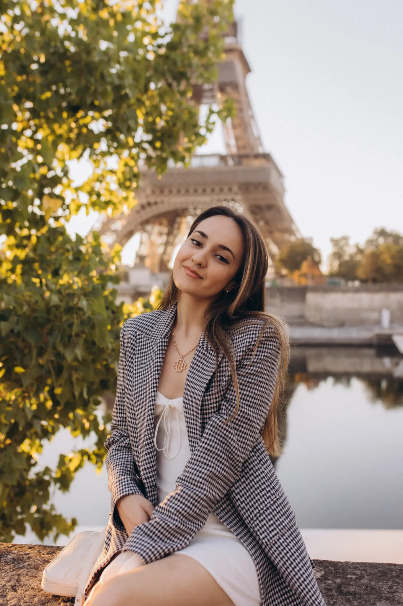 A checked blazer and white dress by the Seine, framed by turning leaves with the Eiffel Tower beyond.