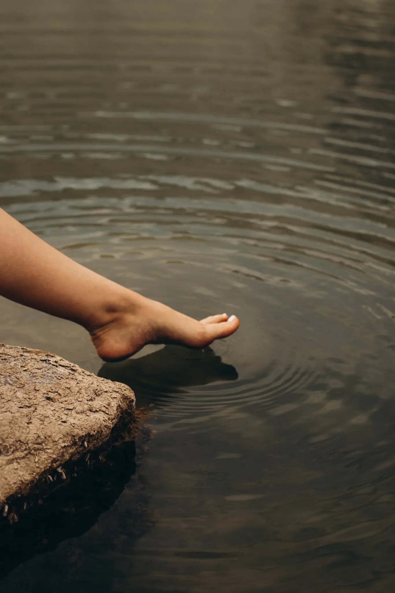 Bare feet touching the water from a stone