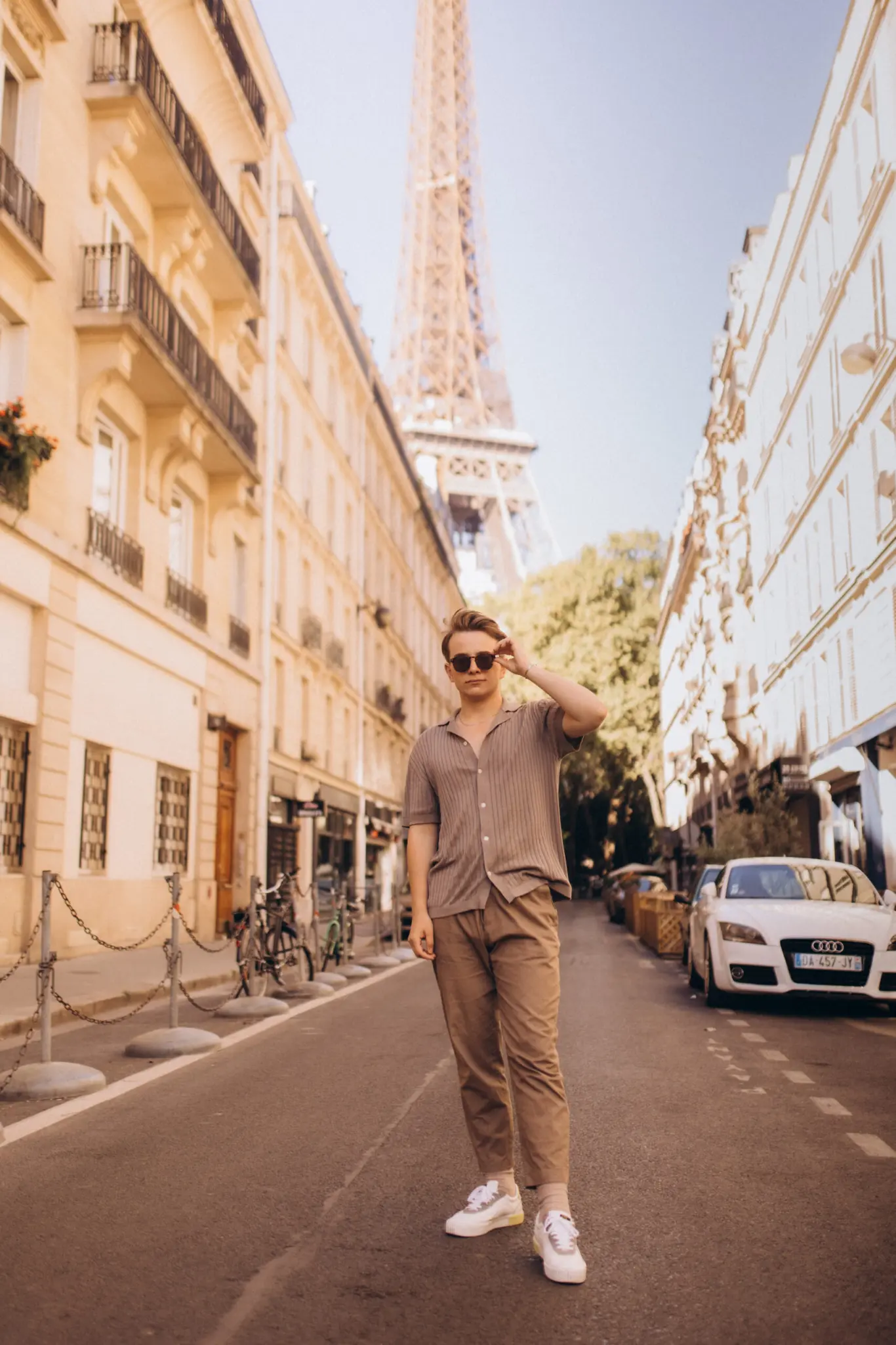Paris street photography, a young man adjusting his sunglasses as he stands on a long Parisian street that frames the iron tower in the distance