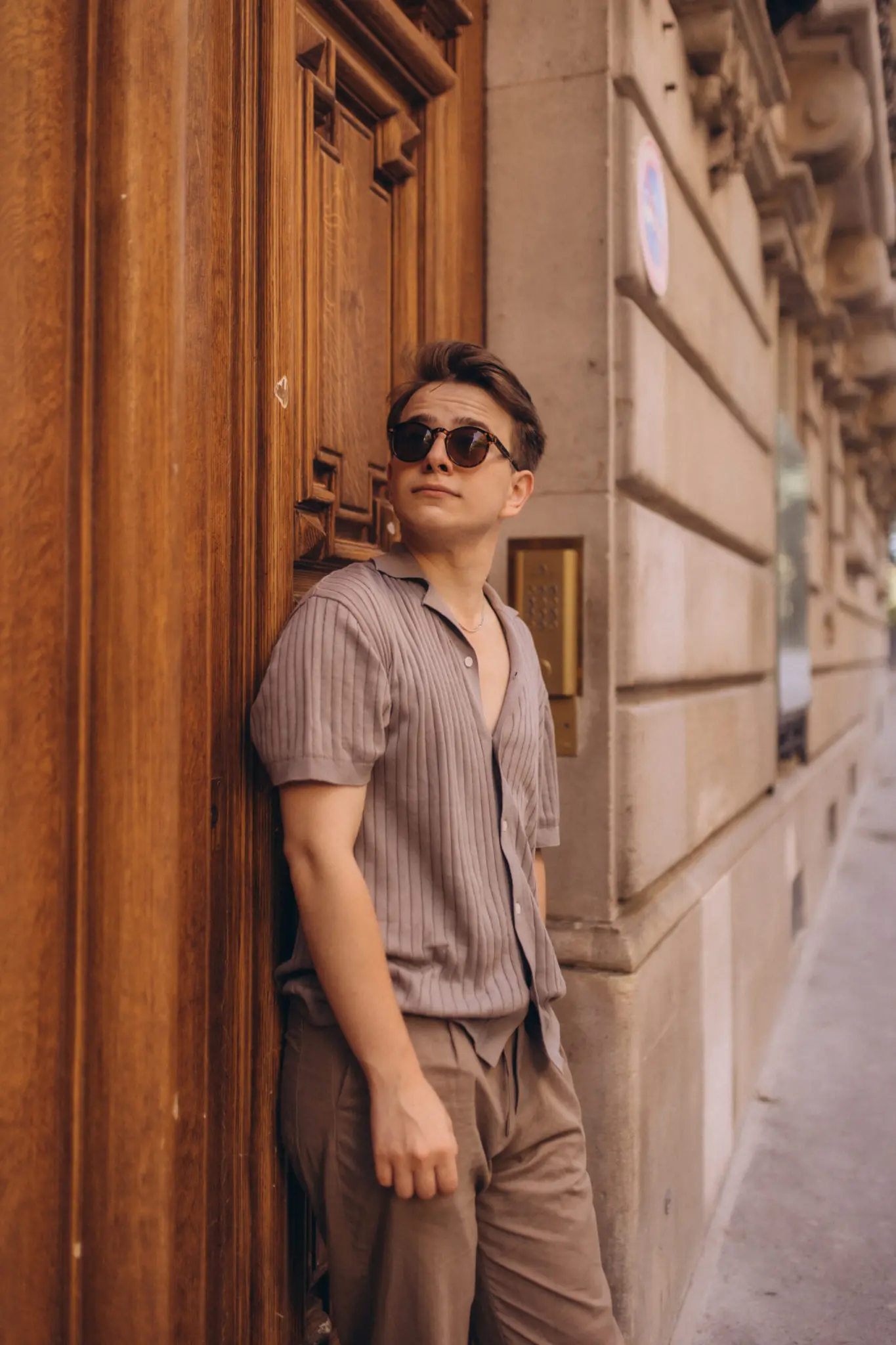 Paris street photography, a young man in sunglasses leaning against a tall carved wooden Parisian door, looking up into the light