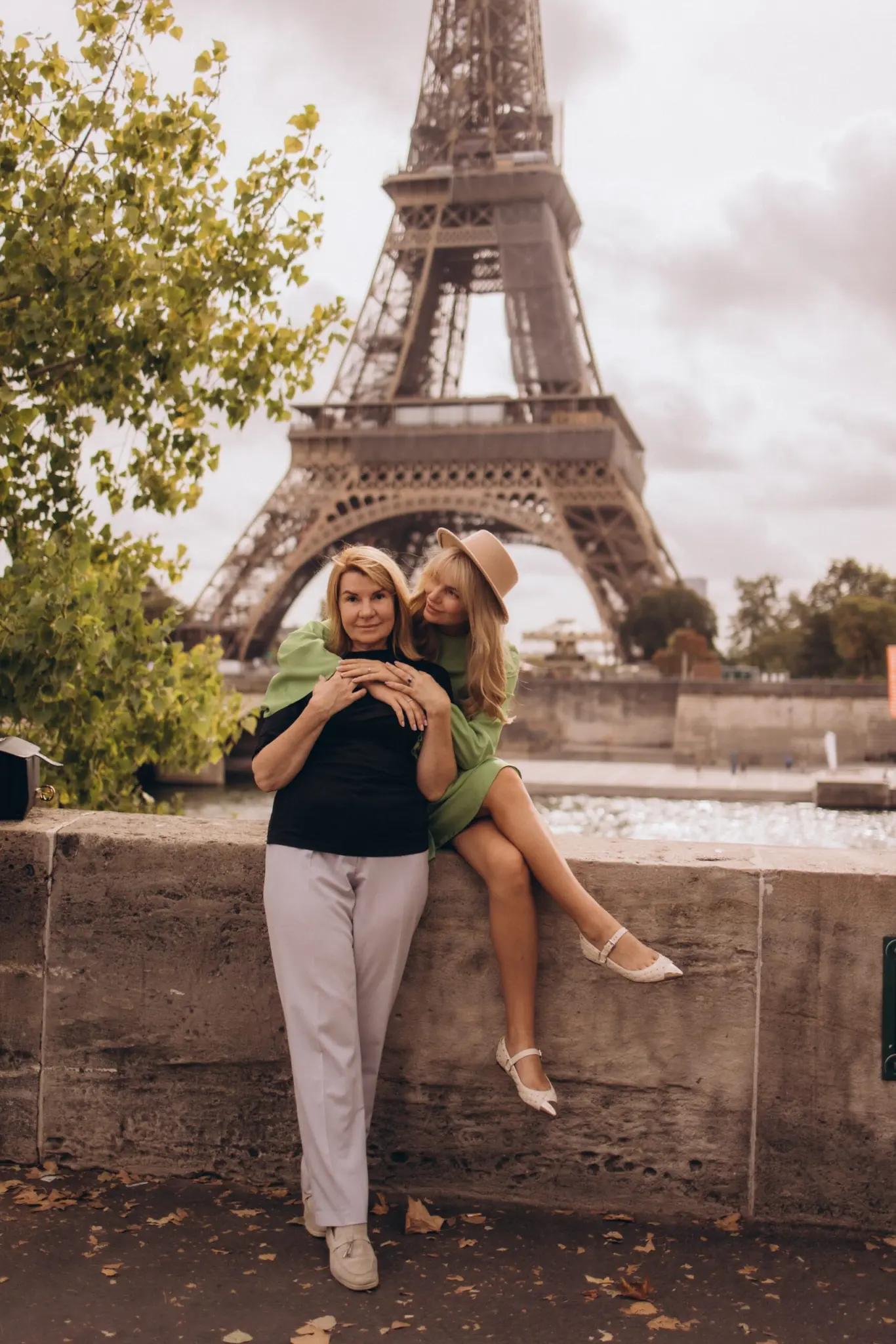 Mother and daughter sitting on a stone wall in front of the Eiffel Tower