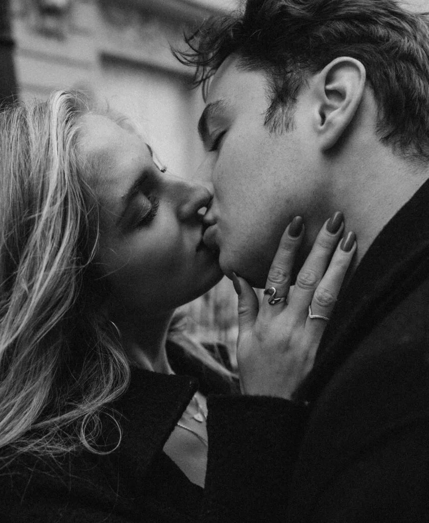 Close-up black and white kiss as the woman cups her partner's face, engagement ring on her hand