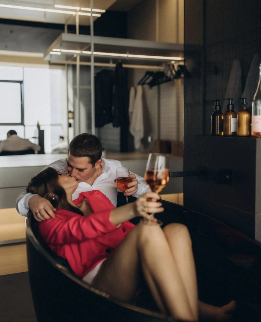 Newly engaged couple sharing a kiss and a glass of rosé in a stylish hotel bathtub during an intimate Paris engagement photoshoot