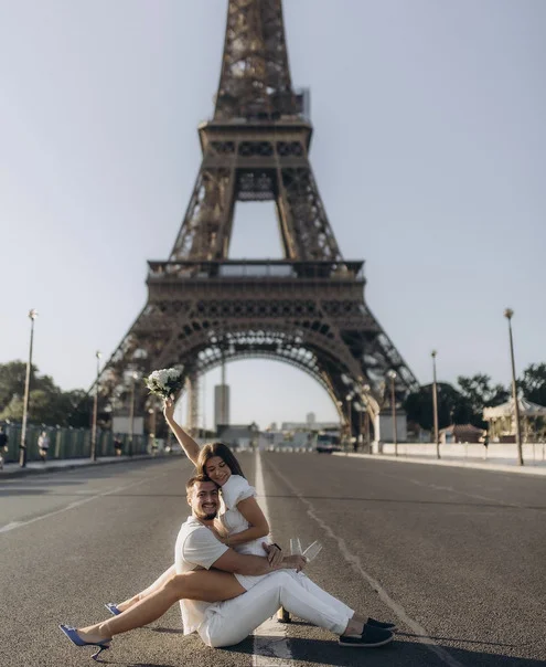 A couple sitting on the road at Bir-Hakeim with a raised bouquet and champagne, taken by a Paris Eiffel Tower photographer