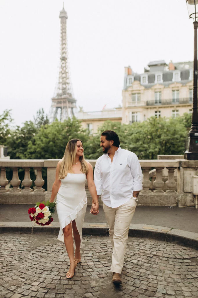 A couple walking hand in hand on cobblestones with a bouquet and the tower behind them, taken by a Paris Eiffel Tower photographer