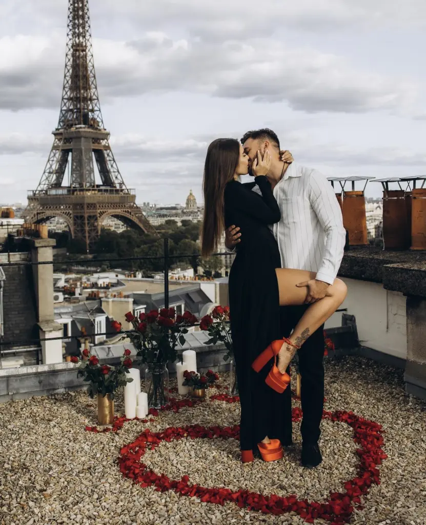 Couple kiss on a rooftop inside a heart of rose petals with the Eiffel Tower rising behind