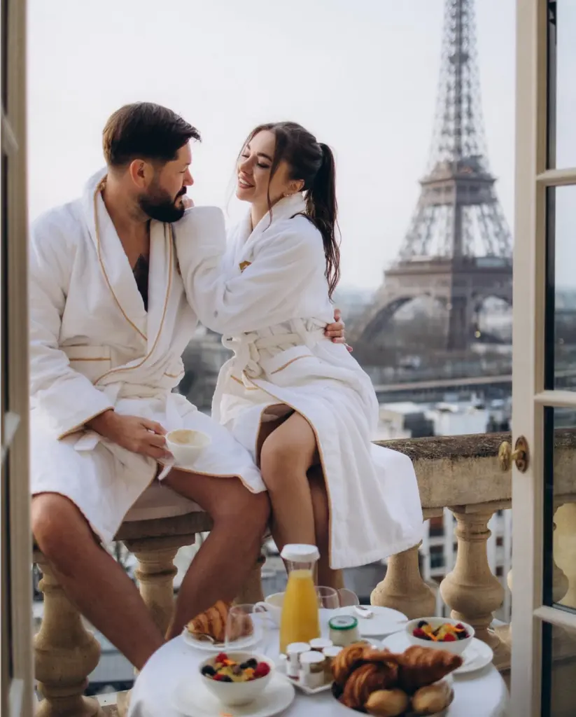 Couple enjoying breakfast in Peninsula hotel with Eiffel Tower view - Paris couple photoshoot on a hotel balcony, a couple in white robes at breakfast with croissants and coffee, by Julia Litvin