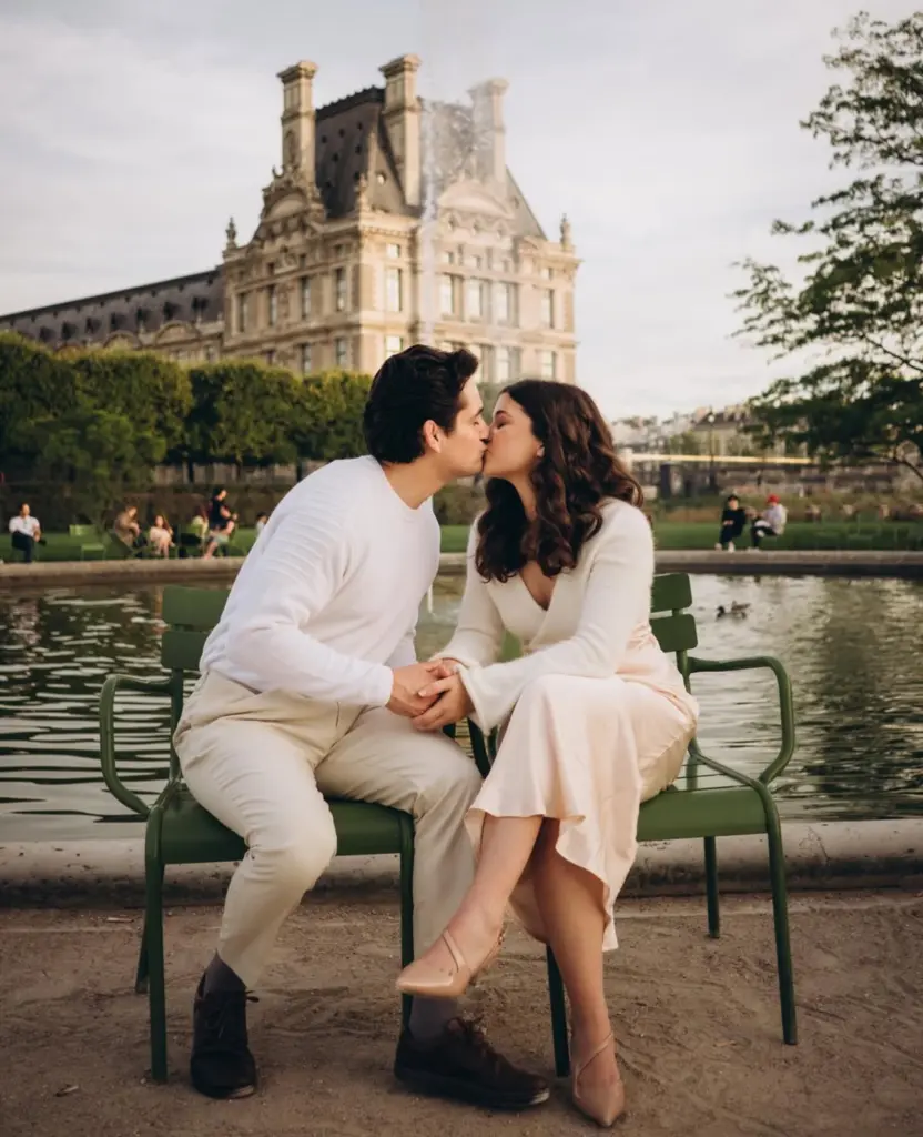 Couple kissing by a pond in Tuileries Garden - Couple photoshoot in the Tuileries Garden, a couple kissing on green chairs by the pond in front of the Louvre, by Julia Litvin