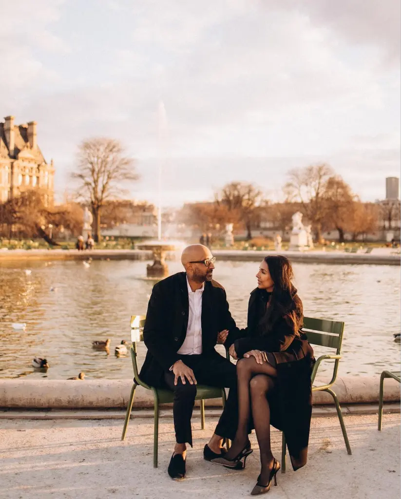 Paris couple photoshoot in winter, a couple in black coats sitting on green chairs by the Tuileries pond, by Julia Litvin
