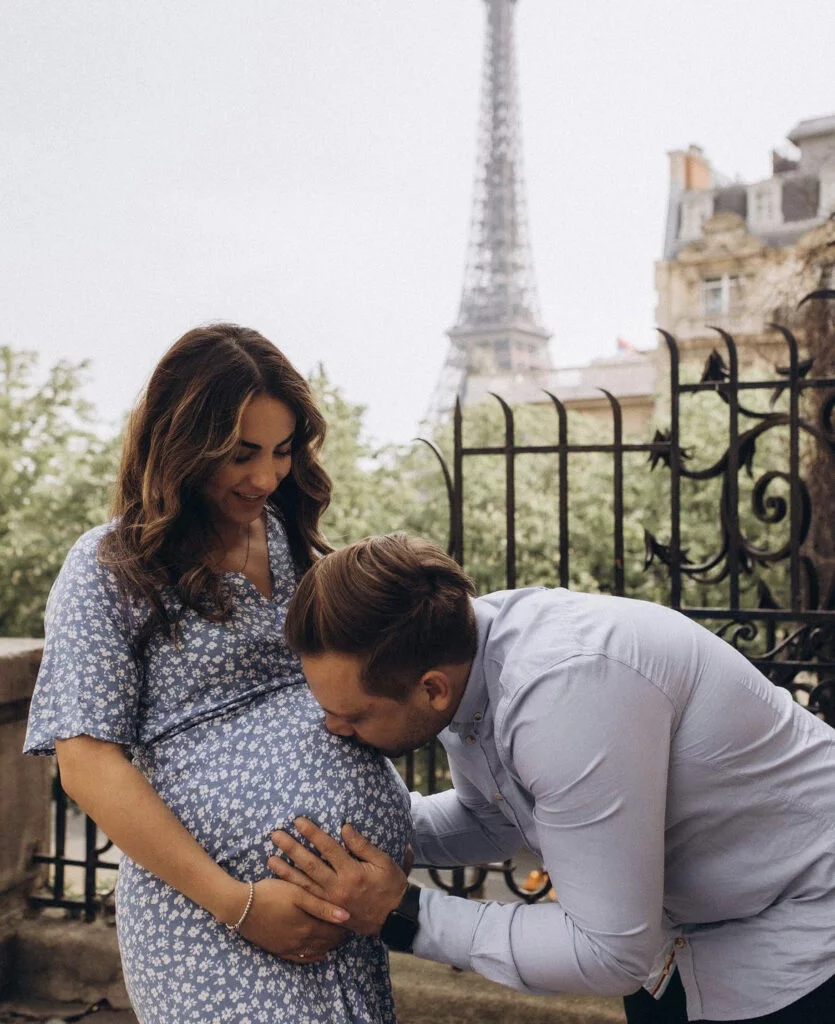 Partner kissing the baby bump at a maternity photoshoot in Paris on a balcony