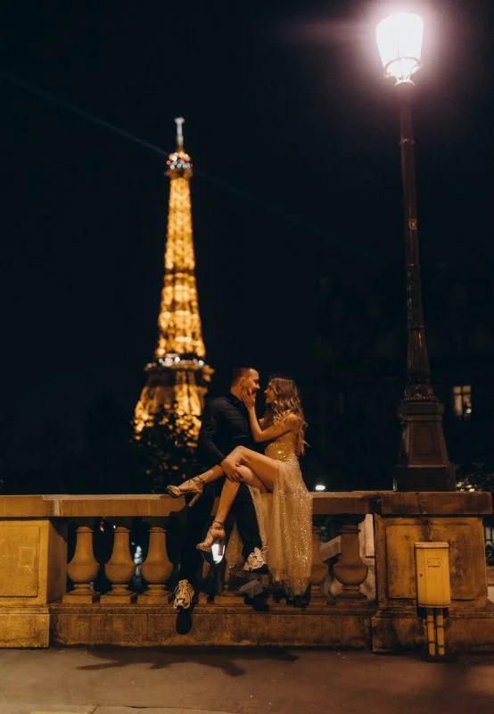 Couple on a stone balustrade at night with the lit Eiffel Tower behind them