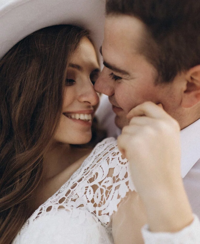 Close-up of a newly engaged couple nose to nose and smiling during a Paris engagement photoshoot with Julia Litvin, the bride-to-be in white lace and a white hat