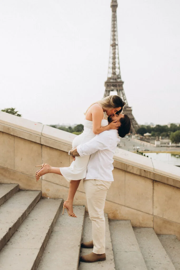 A man lifting his partner for a kiss on the Trocadero steps with the tower behind them during a Paris Eiffel Tower photoshoot