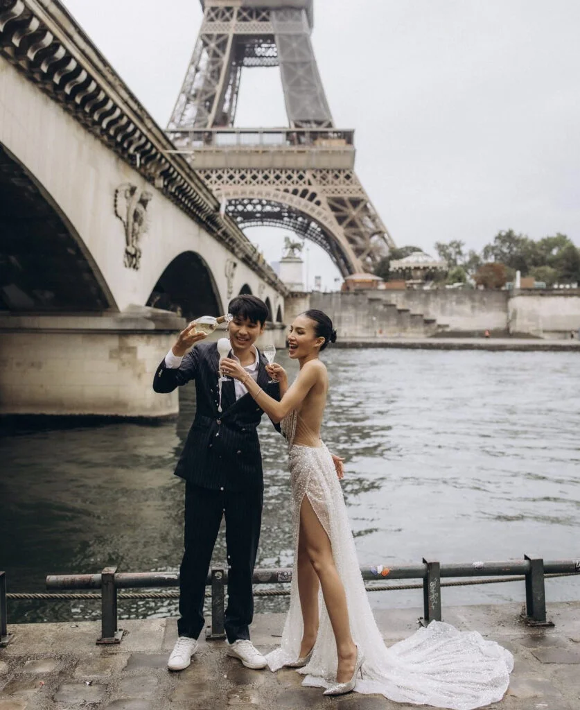 Champagne spilling over with laughter by the river, a Paris engagement photoshoot captured by Julia Litvin at
