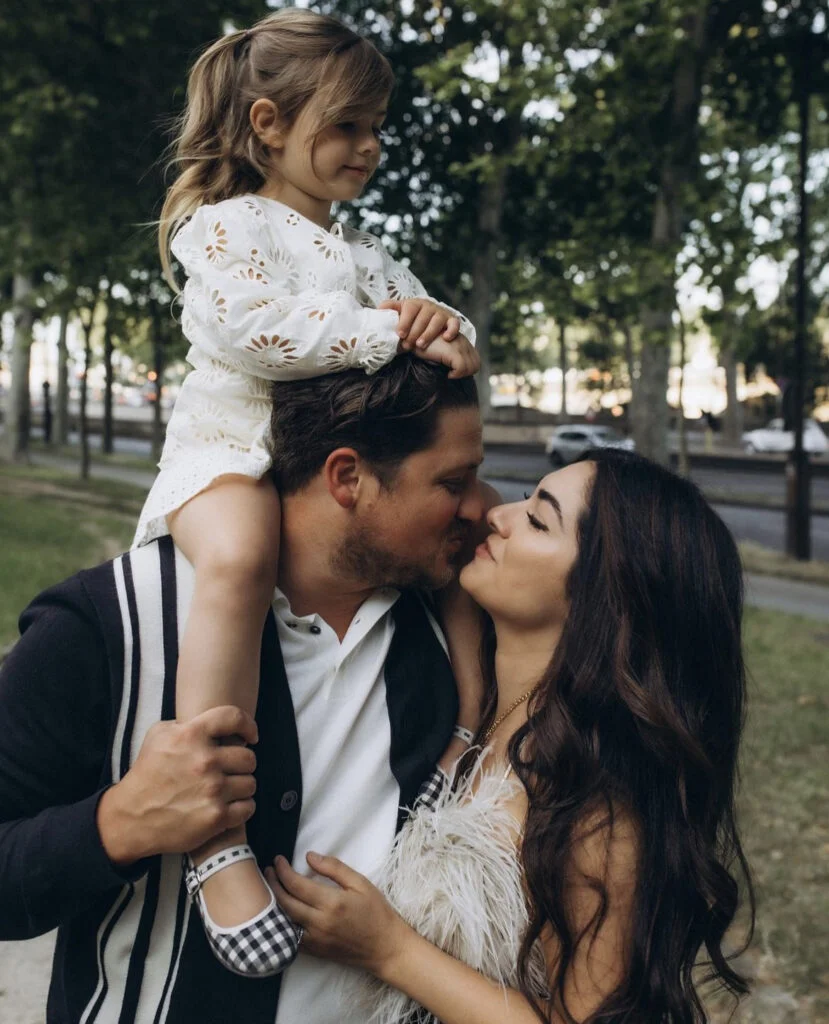Father with his daughter on his shoulders kissing his wife by the Seine in Paris