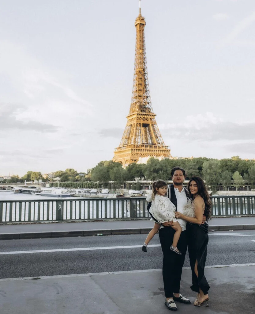 Family of three photographed in Paris at sunset with the river and the iron landmark behind them