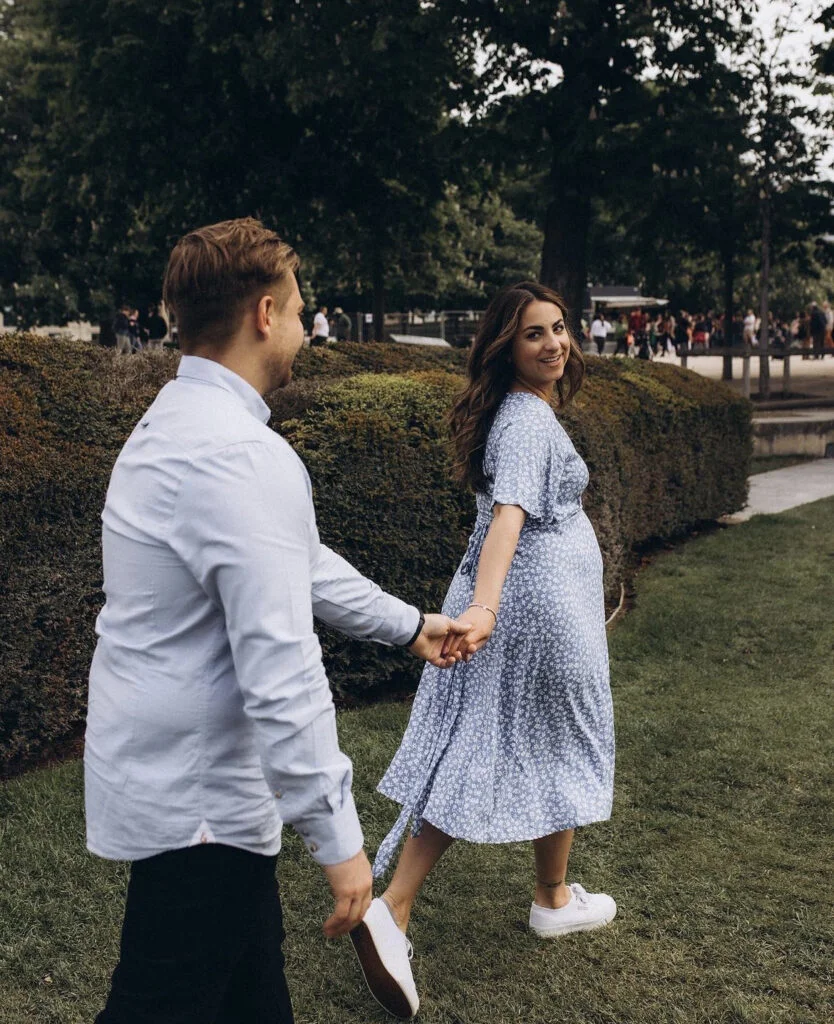 Pregnant woman leading her partner through a Paris park at a maternity photoshoot