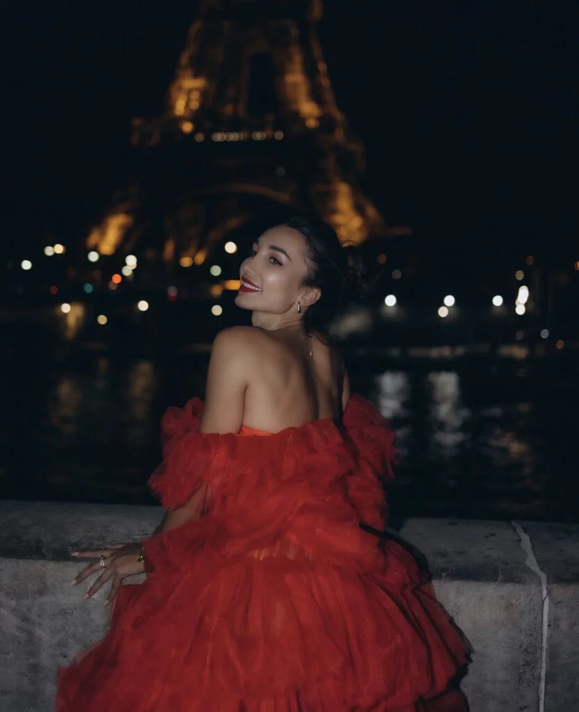 Night portrait photography in Paris, a woman in a red gown looking over her shoulder with the Eiffel Tower glowing behind