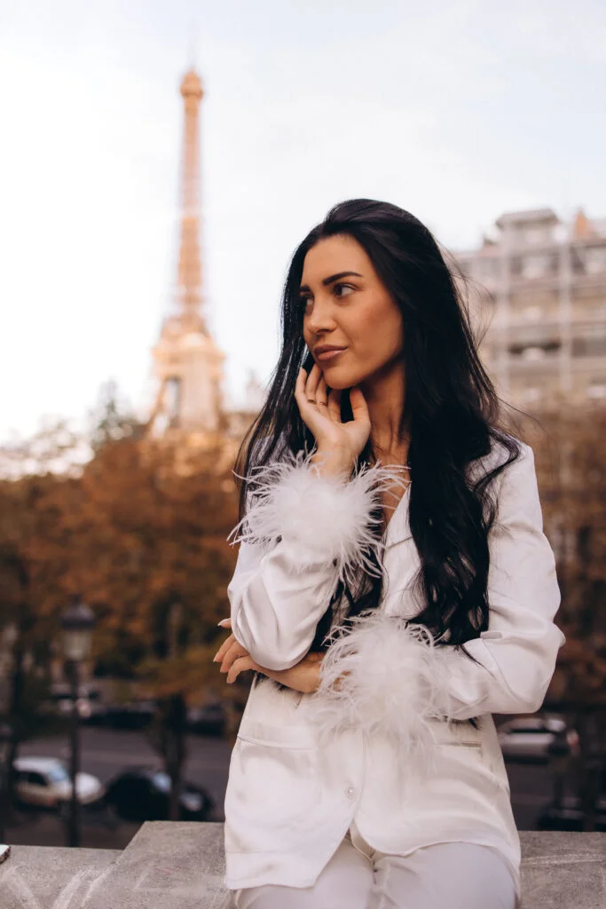 Elegant daytime portrait photography in Paris, a woman in a white feathered suit on a balcony with the Eiffel Tower behind