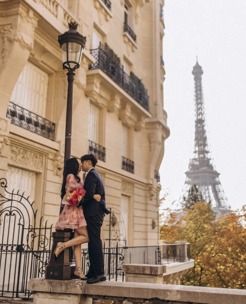 A couple leaning close by a Parisian lamppost on Avenue de Camoens with the tower behind them, taken by an Eiffel Tower photographer