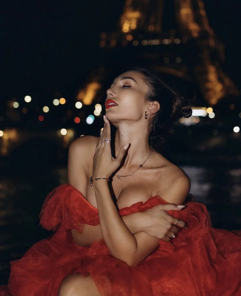 Close-up night portrait photography in Paris, a woman in a red gown with red lips against the glowing Eiffel Tower bokeh