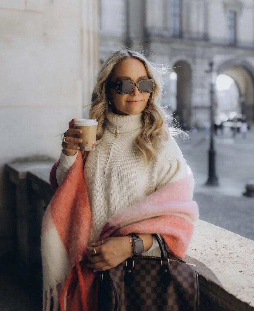 Warm lifestyle portrait photography in Paris, a woman with a coffee cup by a stone colonnade