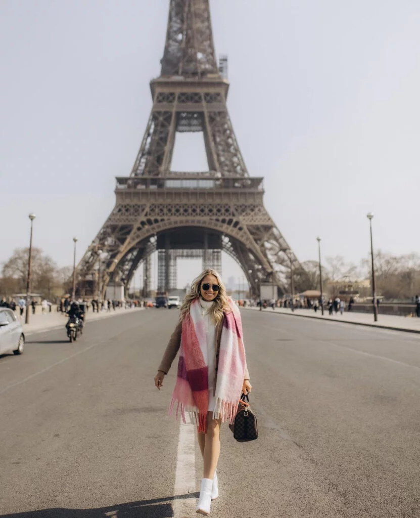 Daytime lifestyle portrait photography in Paris, a woman walking in a pink scarf with the Eiffel Tower behind
