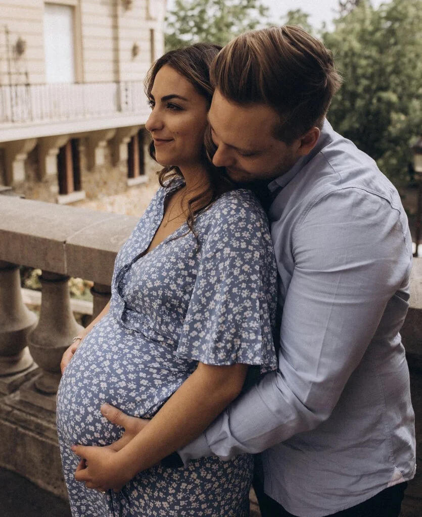Expecting couple embracing by a stone balustrade at a maternity photoshoot in Paris