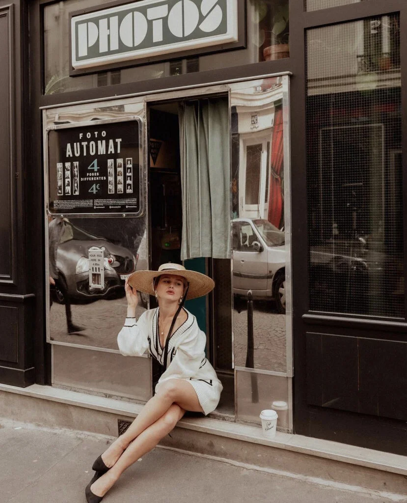 Retro street portrait photography in Paris, a woman in a wide-brimmed hat by a vintage photo booth