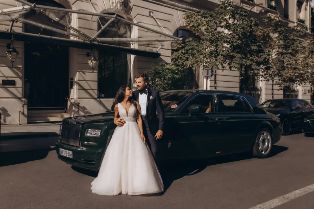Luxury wedding photoshoot in Paris, a bride in a sparkling white gown and a groom in a black tuxedo beside a dark green Rolls-Royce Phantom outside The Peninsula Paris