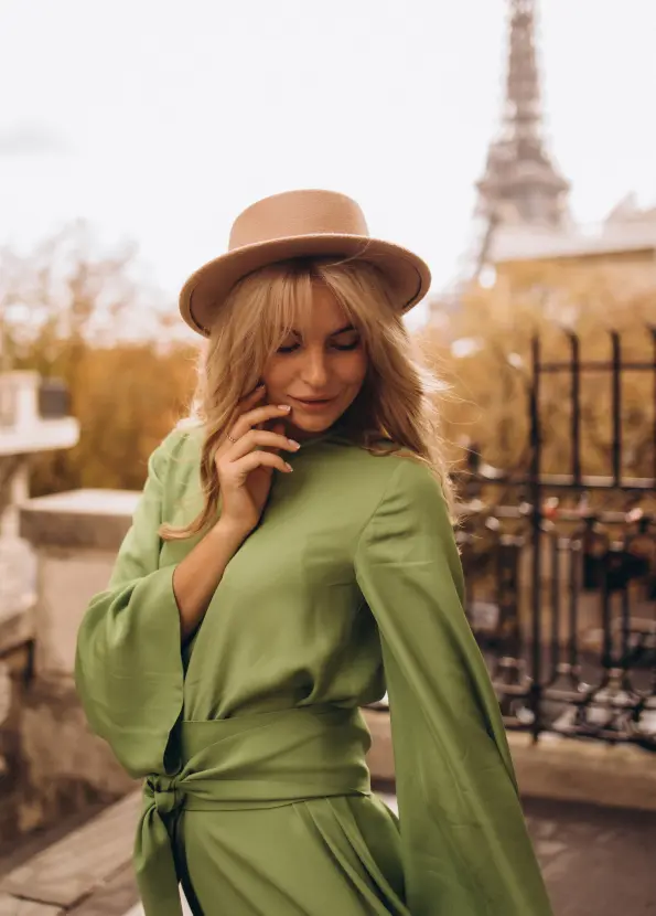 Woman in a green silk dress and a hat posing by a railing with the Eiffel Tower behind her