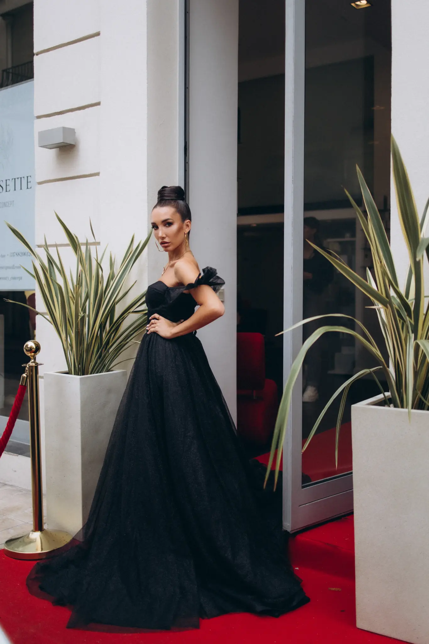 Woman in a black ball gown on a red carpet at a hotel entrance in Cannes