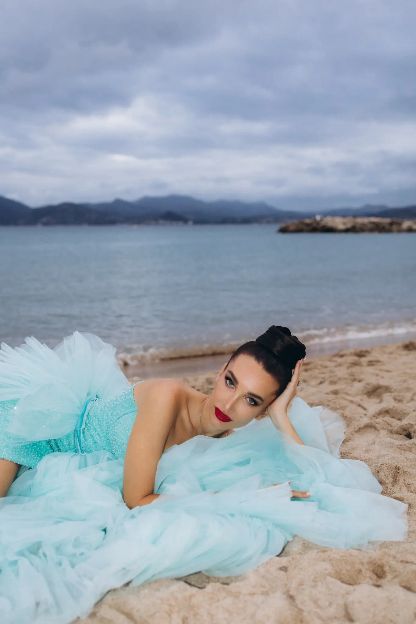 Woman in an aqua tulle gown lying on the sand of a Cannes beach