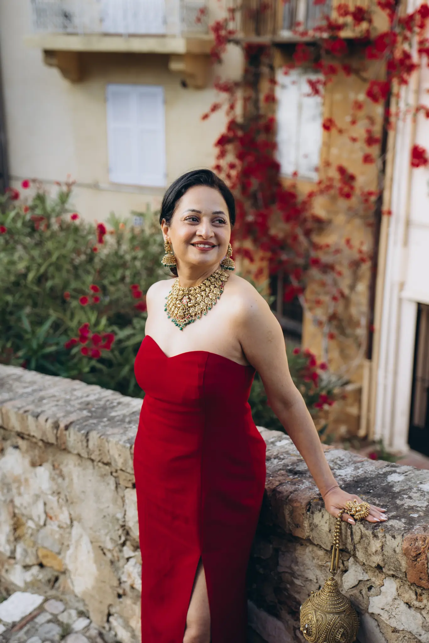 Woman in a red gown by an old stone wall with flowers in Cannes