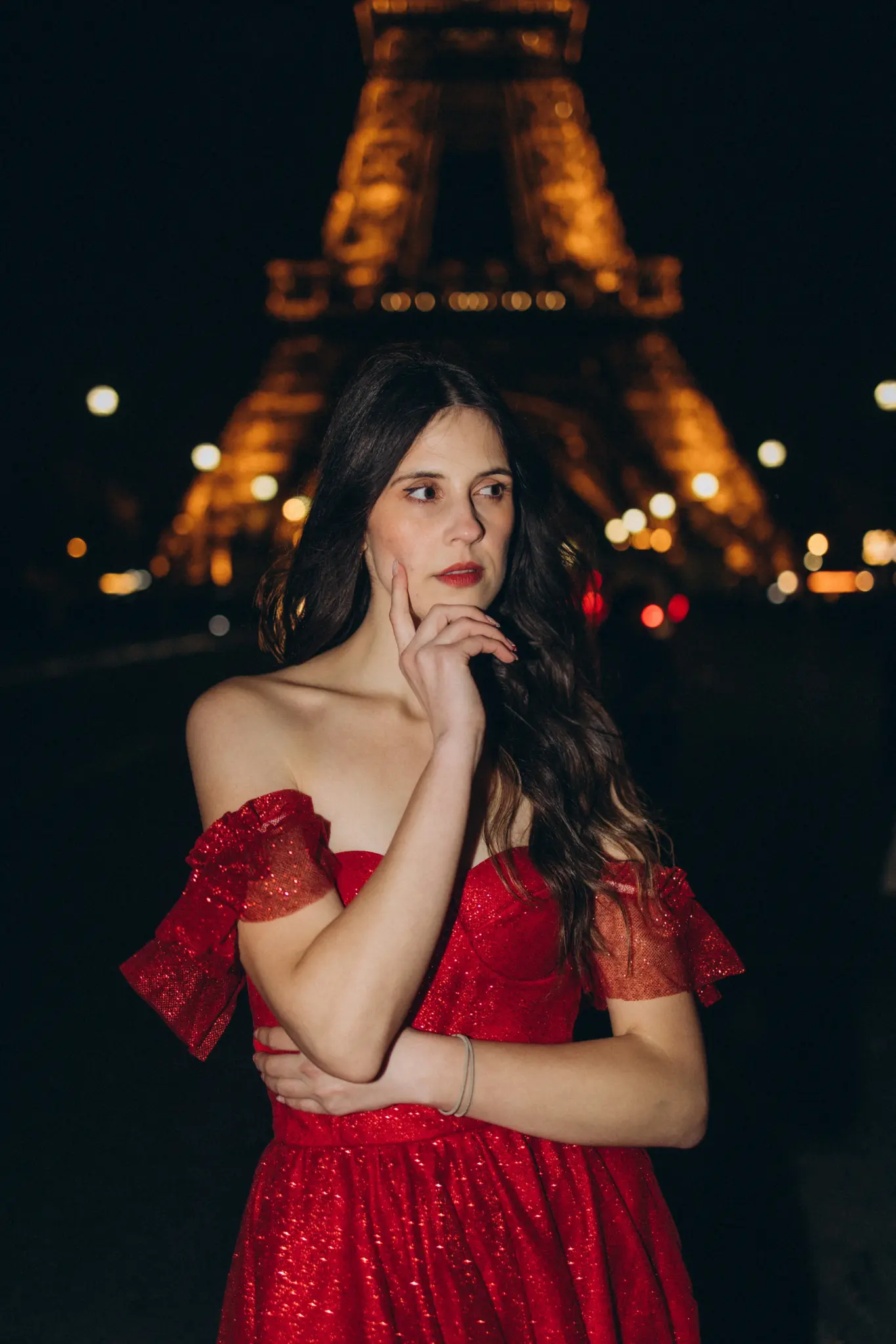 Portrait of a woman in a red off-shoulder gown with the lit Eiffel Tower behind