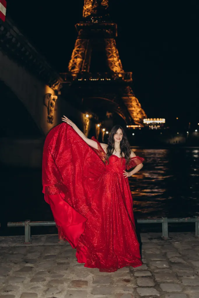 Woman in a red gown twirling on the Seine quay with the illuminated Eiffel Tower