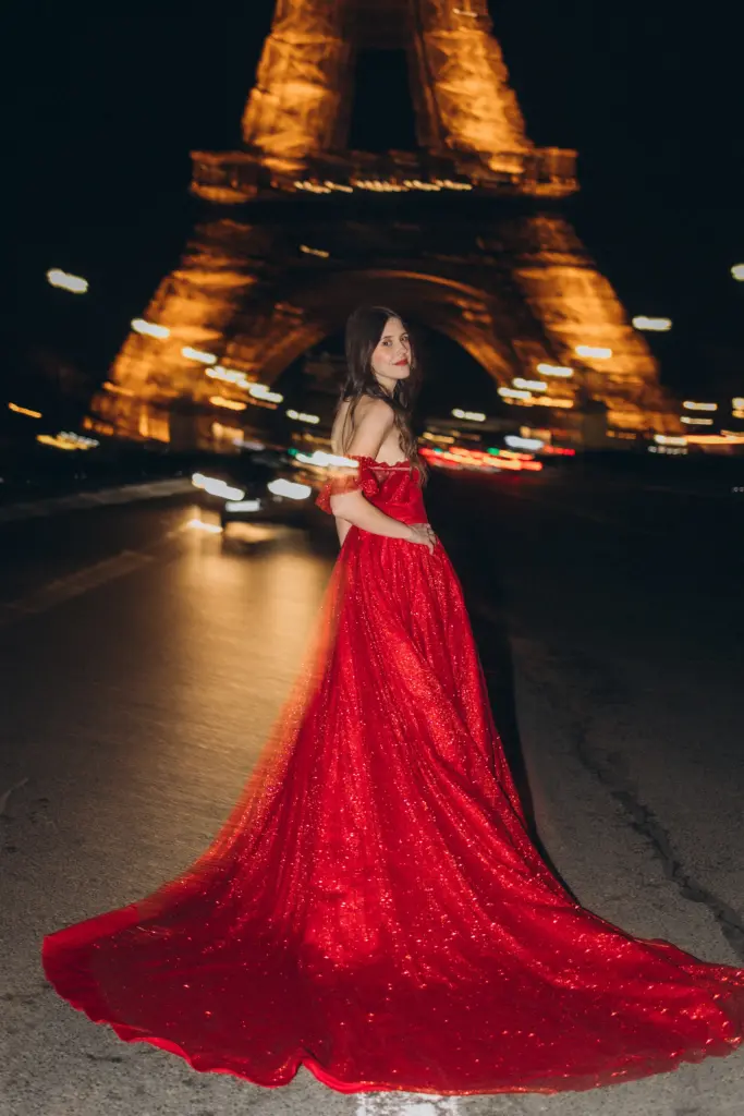 Red gown with a long train spread on the road in front of the lit Eiffel Tower