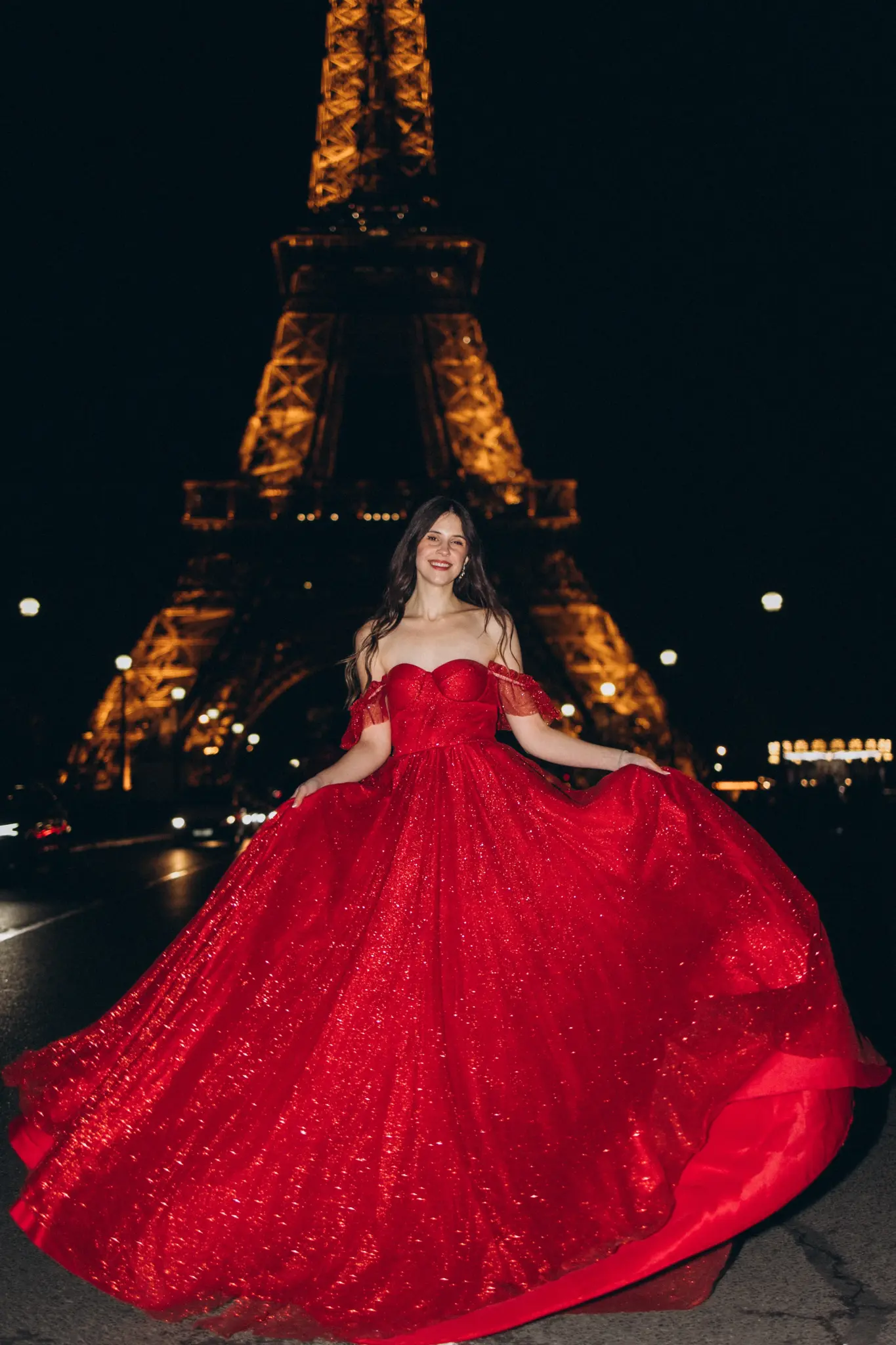 Woman in a red gown twirling in front of the illuminated Eiffel Tower at night