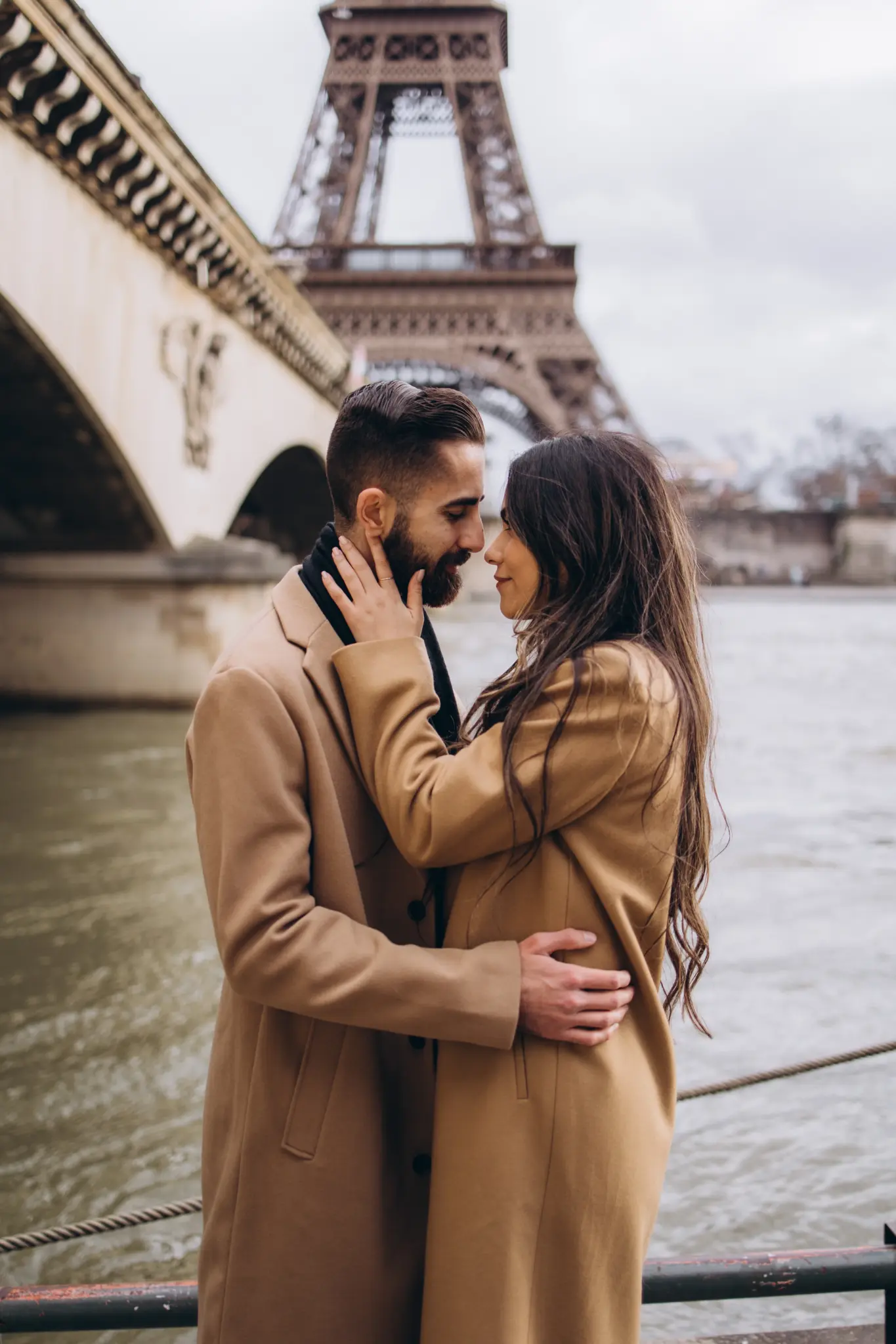 Couple kissing by the stone arches of Pont d’Iéna on the Seine with the Eiffel Tower
