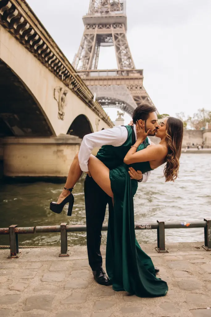 Man dipping a woman in a green gown for a kiss by the Seine with the Eiffel Tower