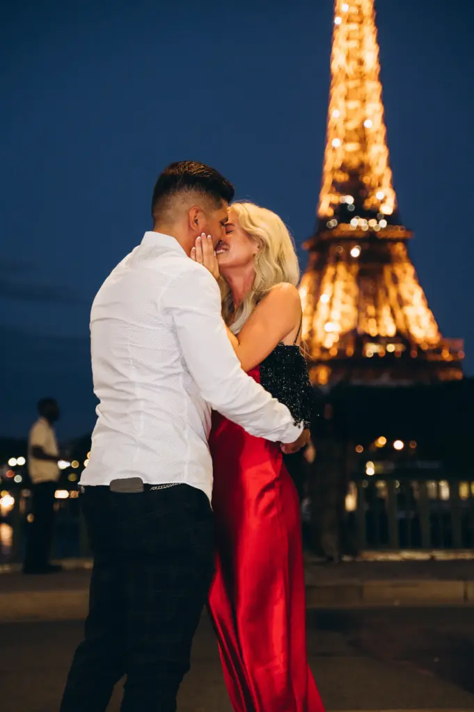 Couple kissing at night, the woman in a red dress, with the lit Eiffel Tower