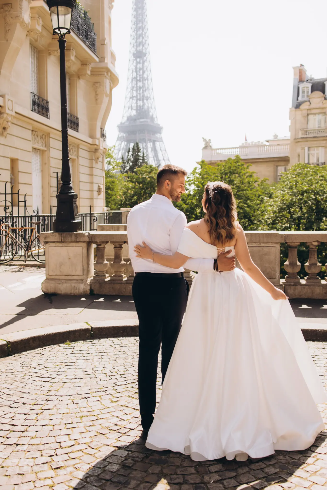 Bride and groom from behind on a cobbled terrace looking toward the Eiffel Tower