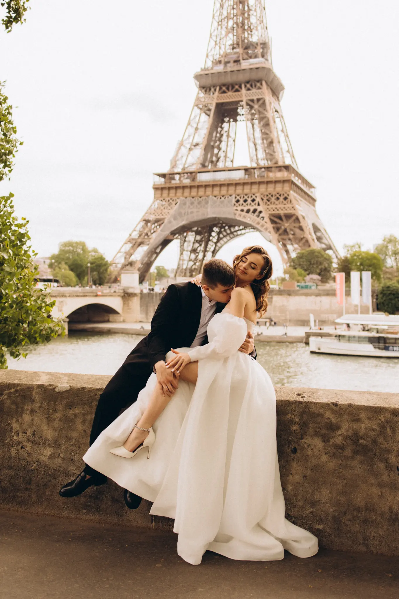 Bride and groom sitting on the river wall with the Eiffel Tower behind
