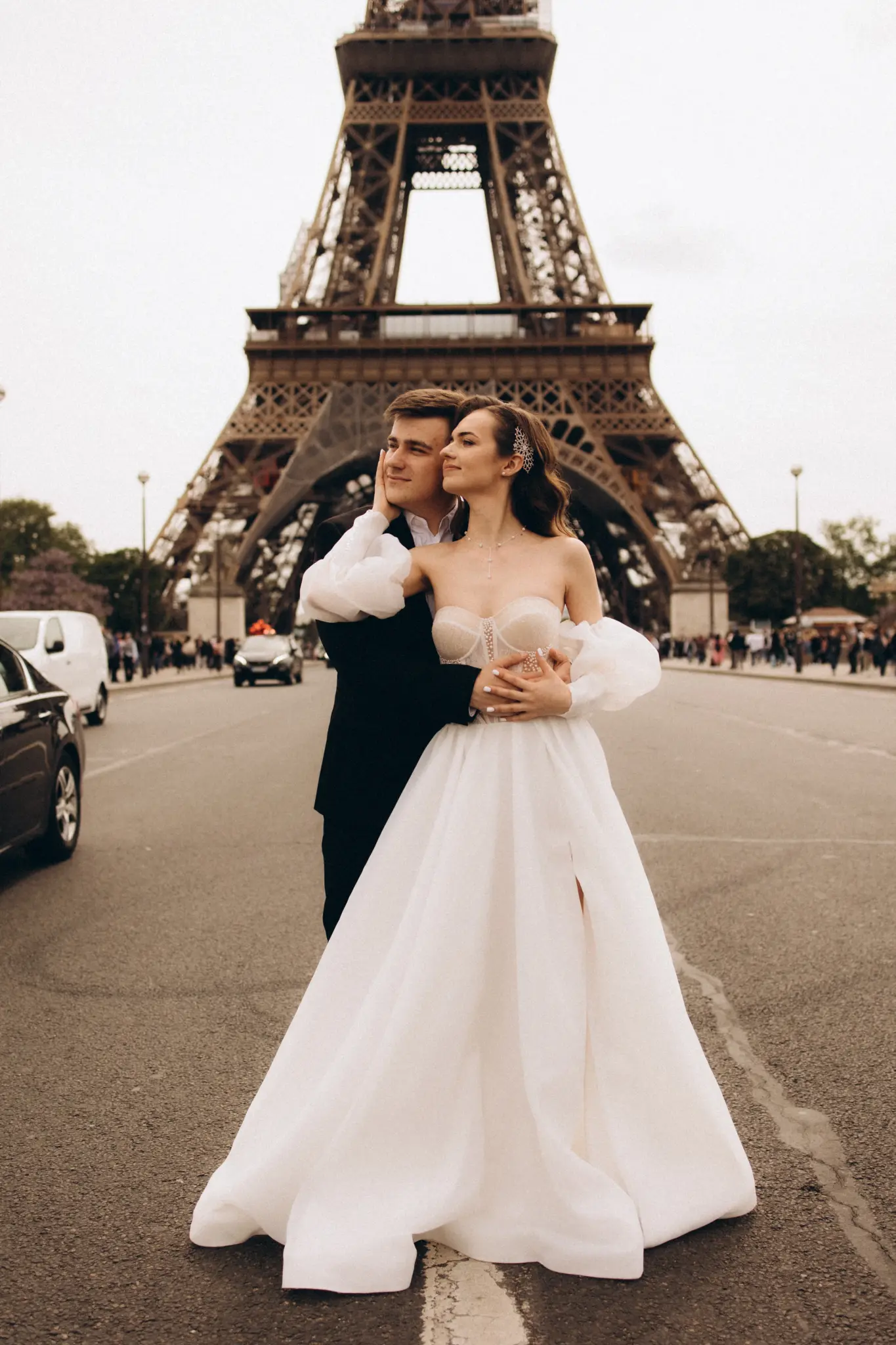 Bride in an off-shoulder gown and groom standing in front of the Eiffel Tower