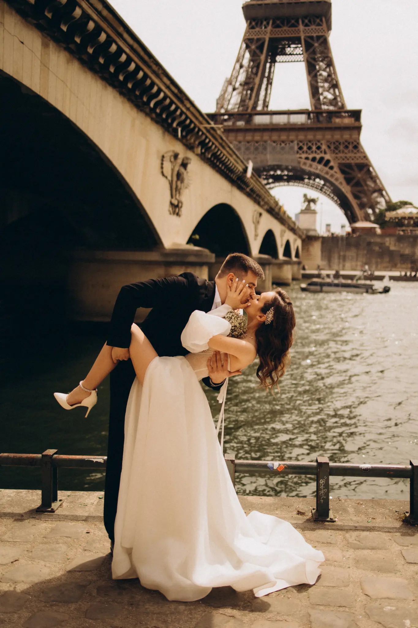 Groom lifting the bride by the Seine with the Eiffel Tower over the bridge