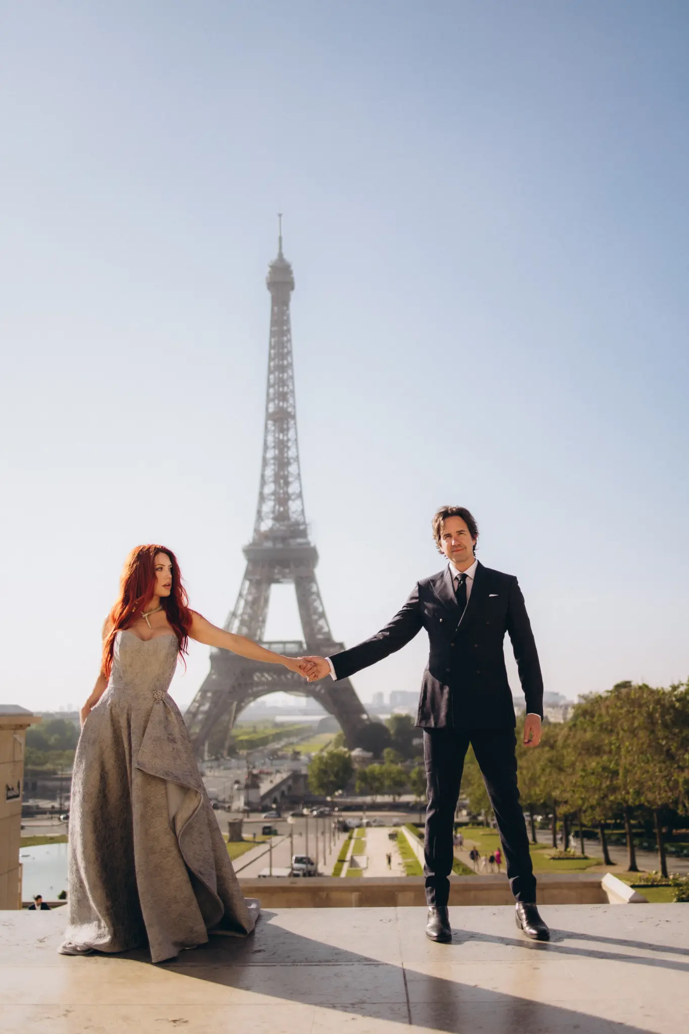 Couple holding hands at Trocadéro, her pale gown flowing, Eiffel Tower behind