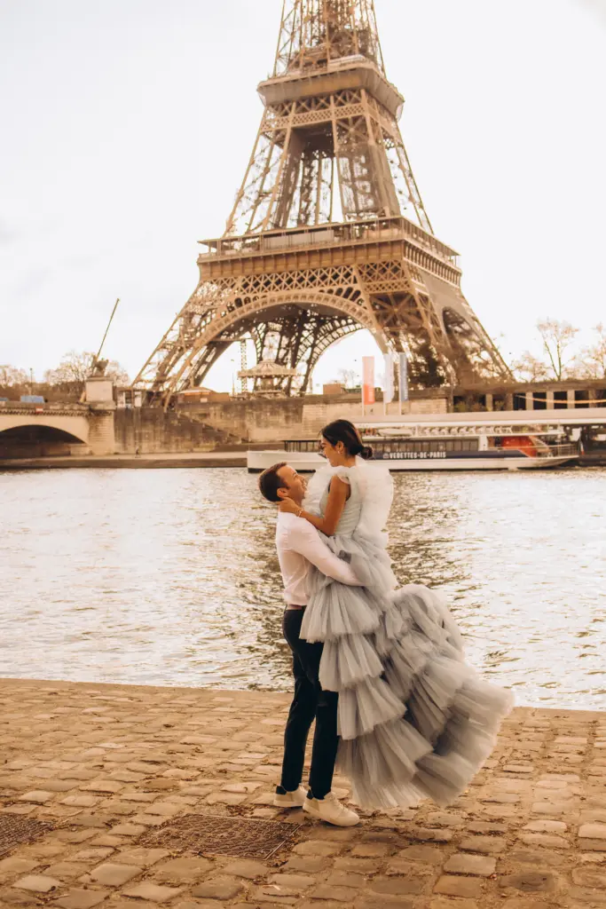 Groom spinning the bride in a tiered tulle gown on the Seine quay below the Eiffel Tower