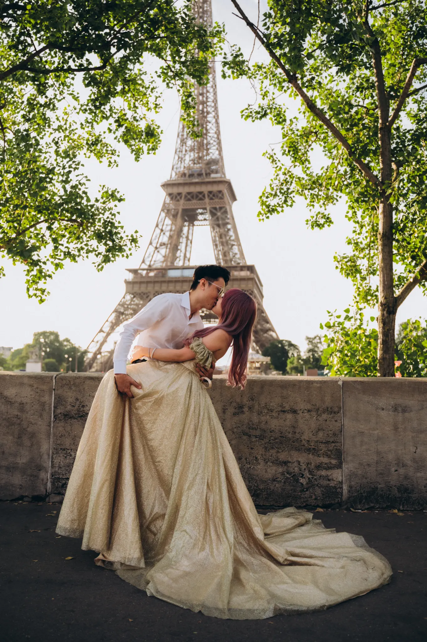 Kiss under the trees with the Eiffel Tower, her golden gown spread on the ground